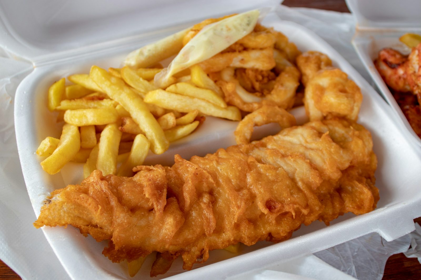 Beer Battered Fish, cooked meat and French fries in white disposable plate